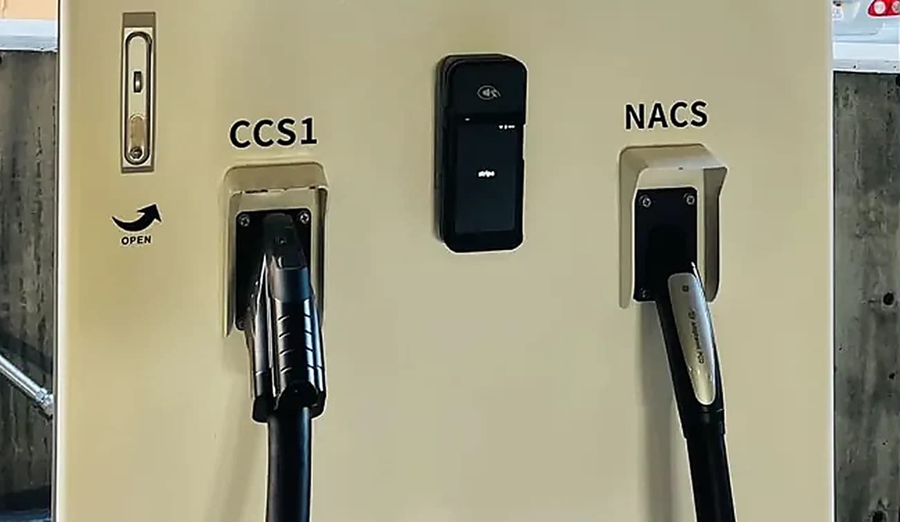 The two cables on a HubCharge charger at Alhambra. The holster on the left is labelled CCS1 and holds a noticeably chunkier plug; the one on the right is labelled NACS and holds a slimmer plug. A card reader sits between them.