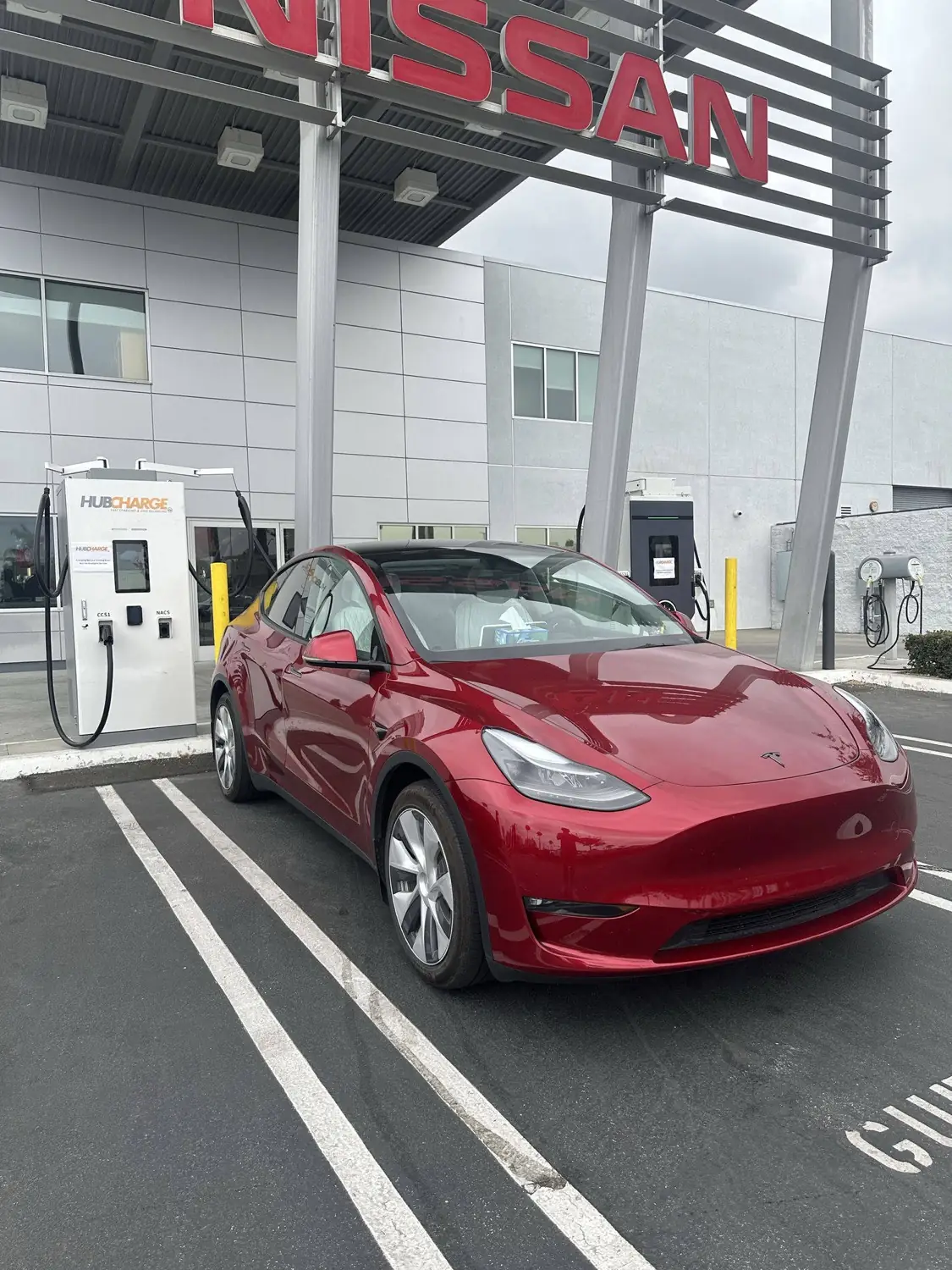 A red Tesla Model Y charging at the HubCharge station outside Fontana Nissan